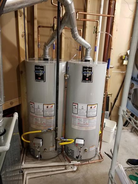 Two water heaters in a utility room with exposed pipes and venting.