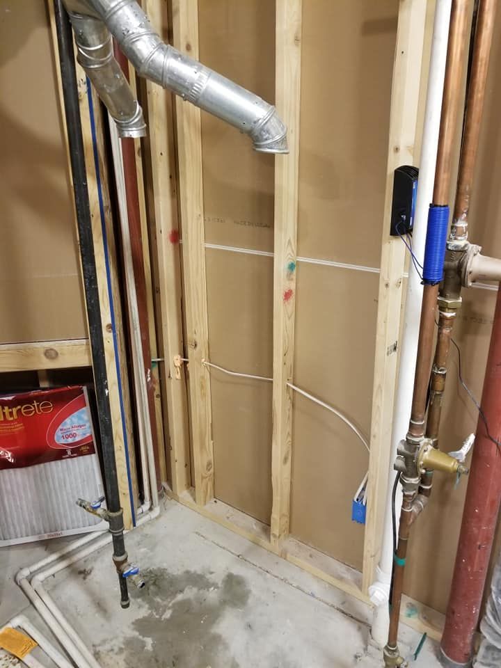 Exposed plumbing and ductwork in a partially renovated wall with bare studs and concrete floor