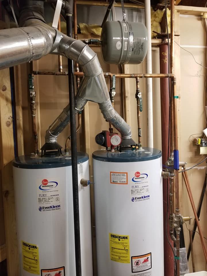 Two white water heaters with silver vent pipes in a utility room