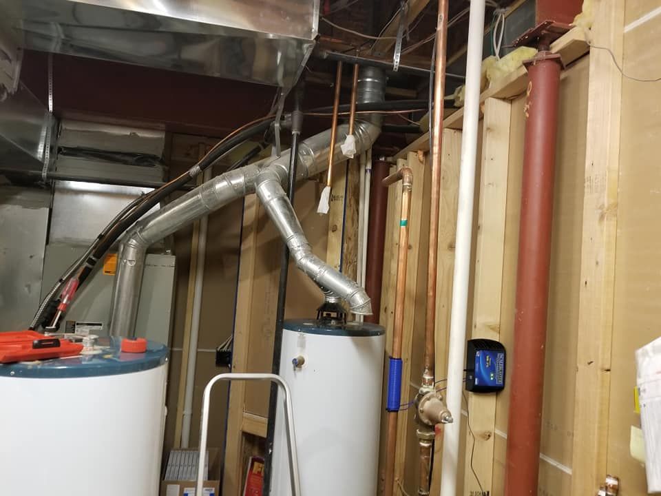 Basement mechanical room with water heaters, metal ducts, pipes, and exposed framing