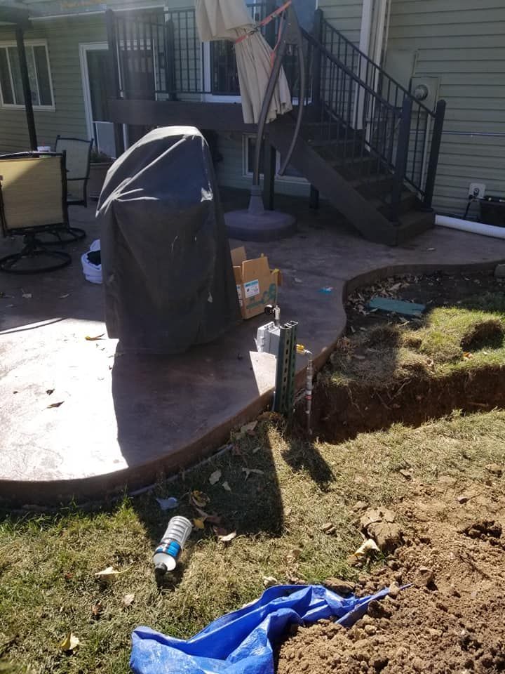 Backyard patio with covered grill, stairs, and scattered items on grass and concrete.