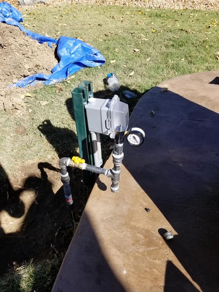 Sprinkler valve assembly on a wooden board in a grassy yard, with blue tarp in the background