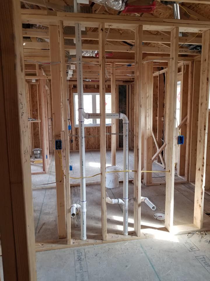 Interior of a house under construction with exposed wooden framing and plumbing pipes.