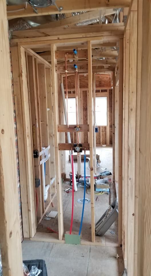 Wood-framed hallway under construction with exposed wiring, pipes, and tools on the floor.