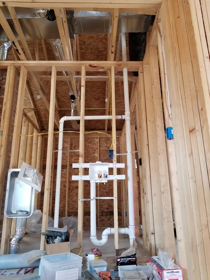 Interior construction site with exposed wood framing, plumbing pipes, and building materials.