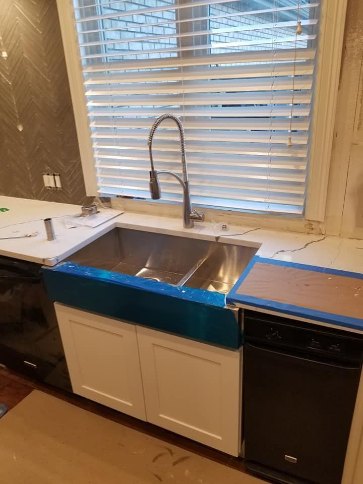 Kitchen sink beneath window with white blinds, blue tape on counter, and dishwasher below