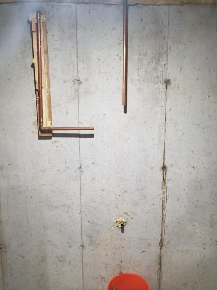 Concrete wall with exposed pipes and a red bucket at the bottom.