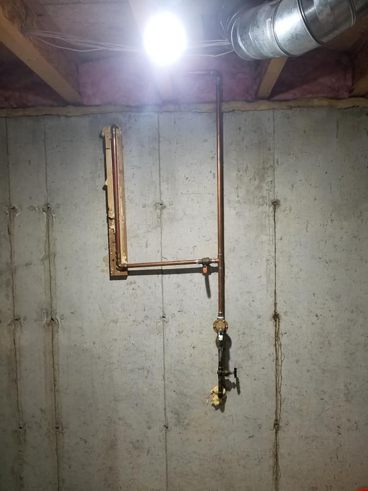 Basement wall with exposed copper pipes, a hanging valve, and a bright utility light above.