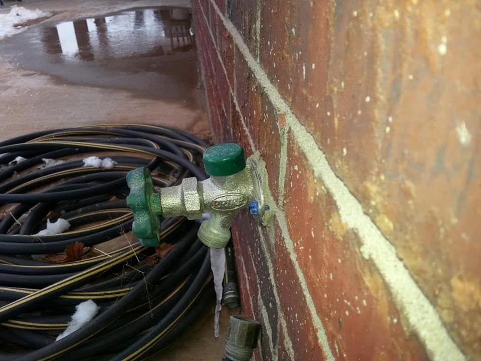 Coiled black hoses connected to a green valve on a rusted wall in a wet industrial area