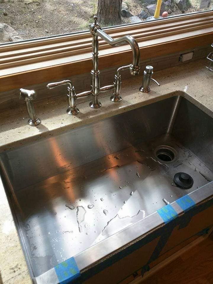 Stainless steel kitchen sink with faucet and soap dispensers beneath a window