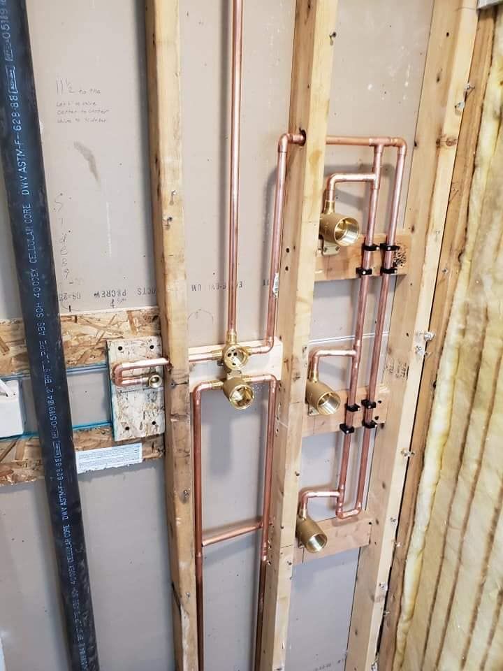 Open wall with exposed copper and black plumbing pipes and valves in a utility area