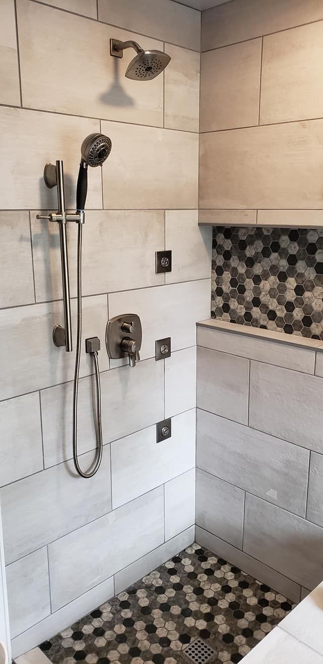 Bathroom shower with white tile walls, handheld showerhead, and pebble mosaic floor and accent strip