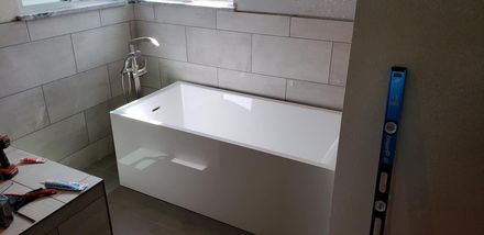 White bathtub installed in a tiled bathroom corner, with a shower fixture and a blue spirit level nearby
