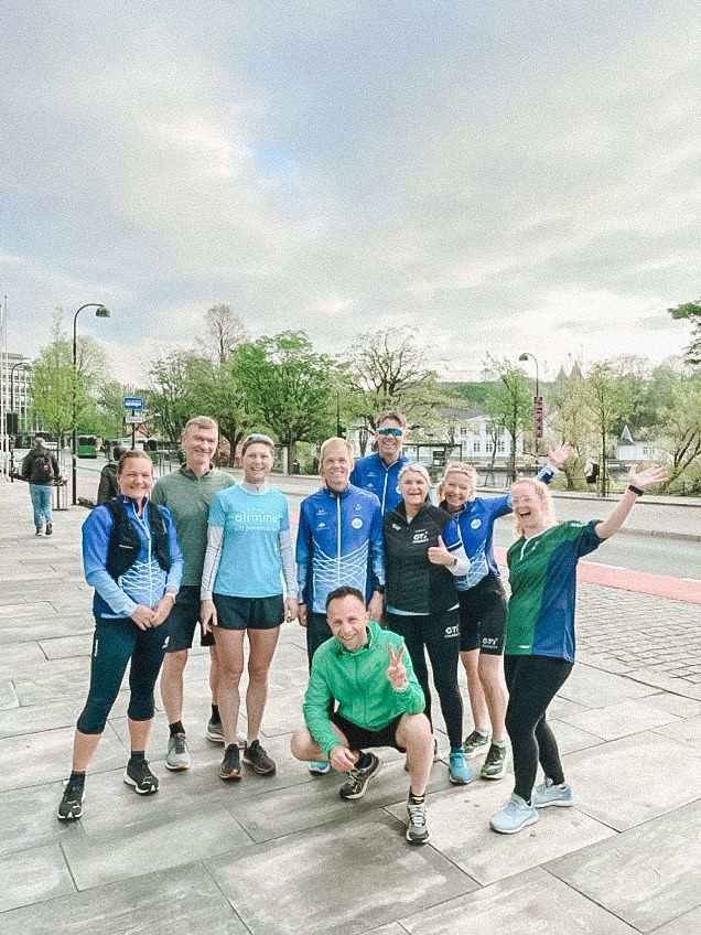 Group of runners in athletic wear posing outside; cloudy sky.