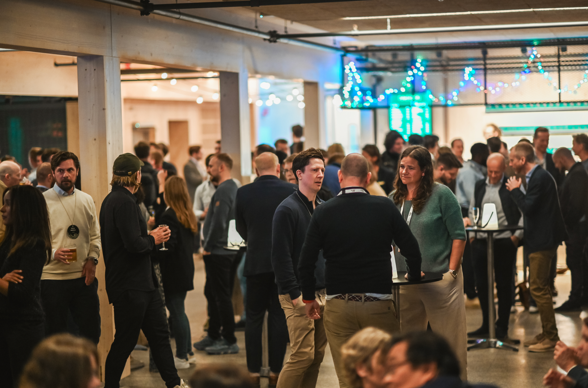 People networking at an event in a large, open industrial-style room.