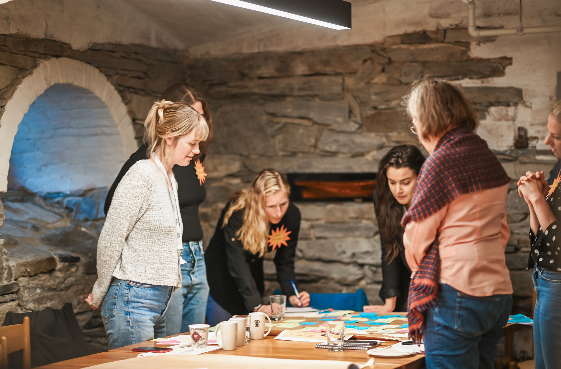 People gather around a table, collaborating and writing in a rustic room.