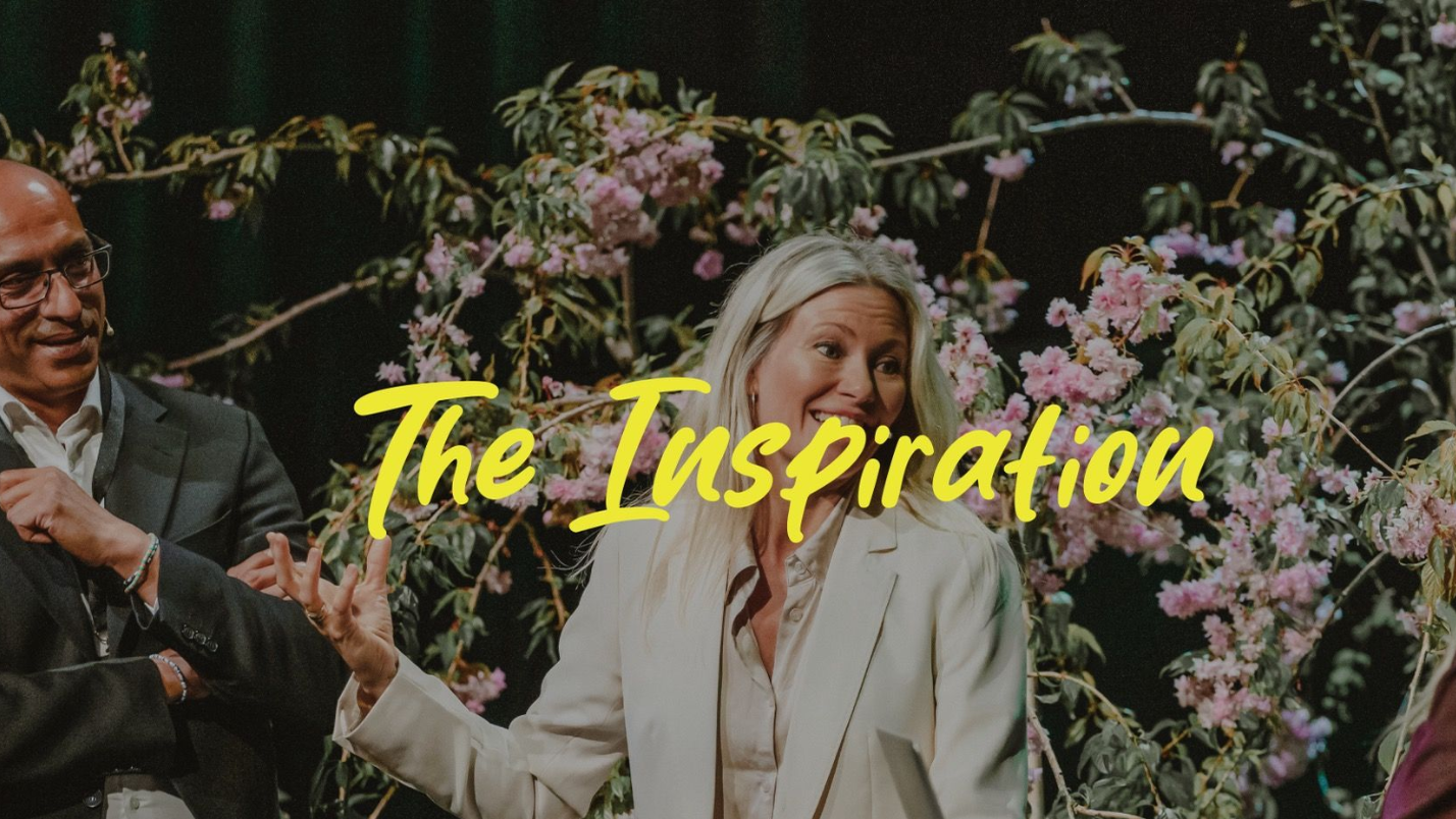Woman in white blazer speaks at event, with floral backdrop, text 
