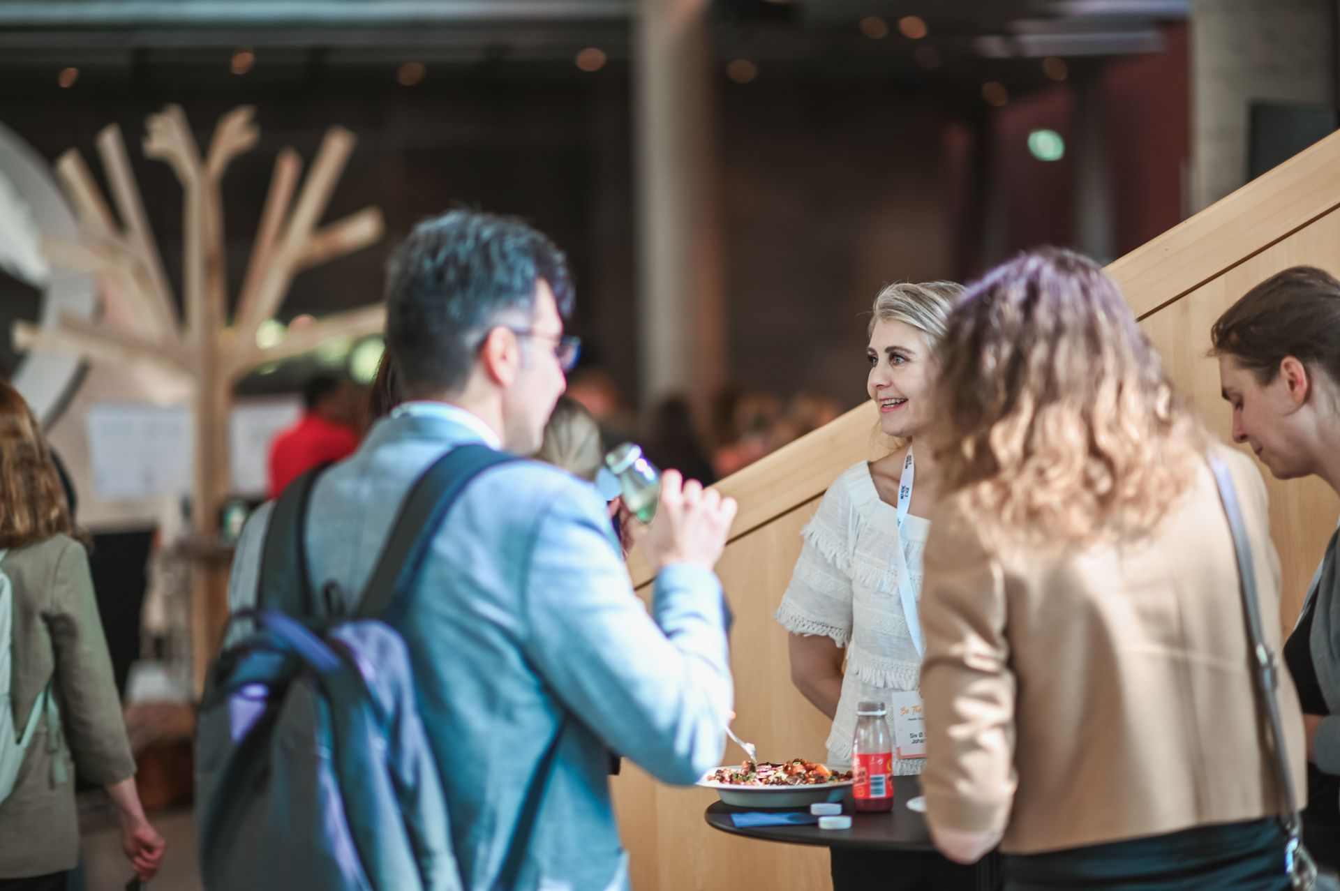 People at a networking event, conversing near a snack table and modern wooden decor.