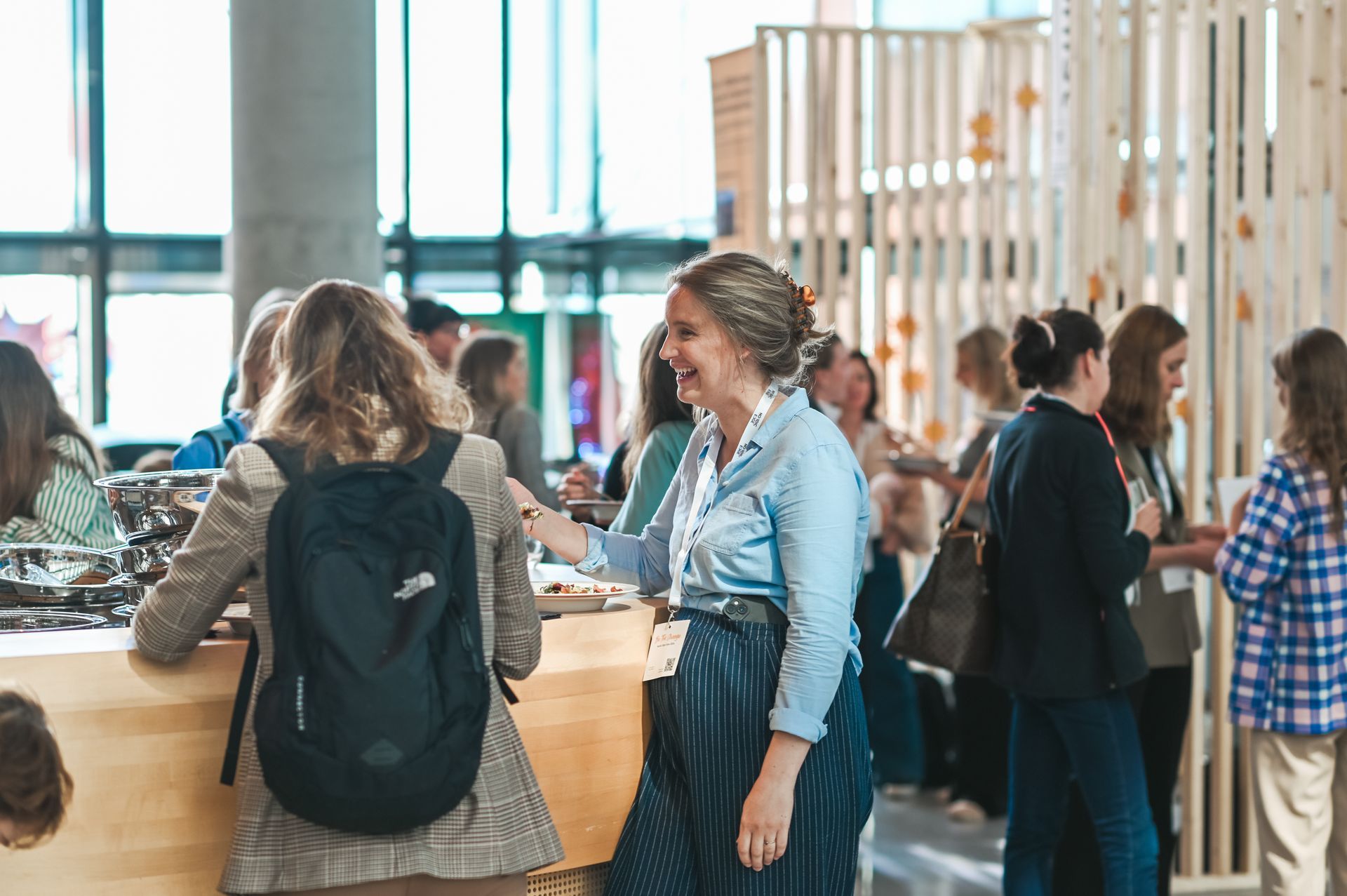 People at an event, some smiling and talking. Wooden structure in background.