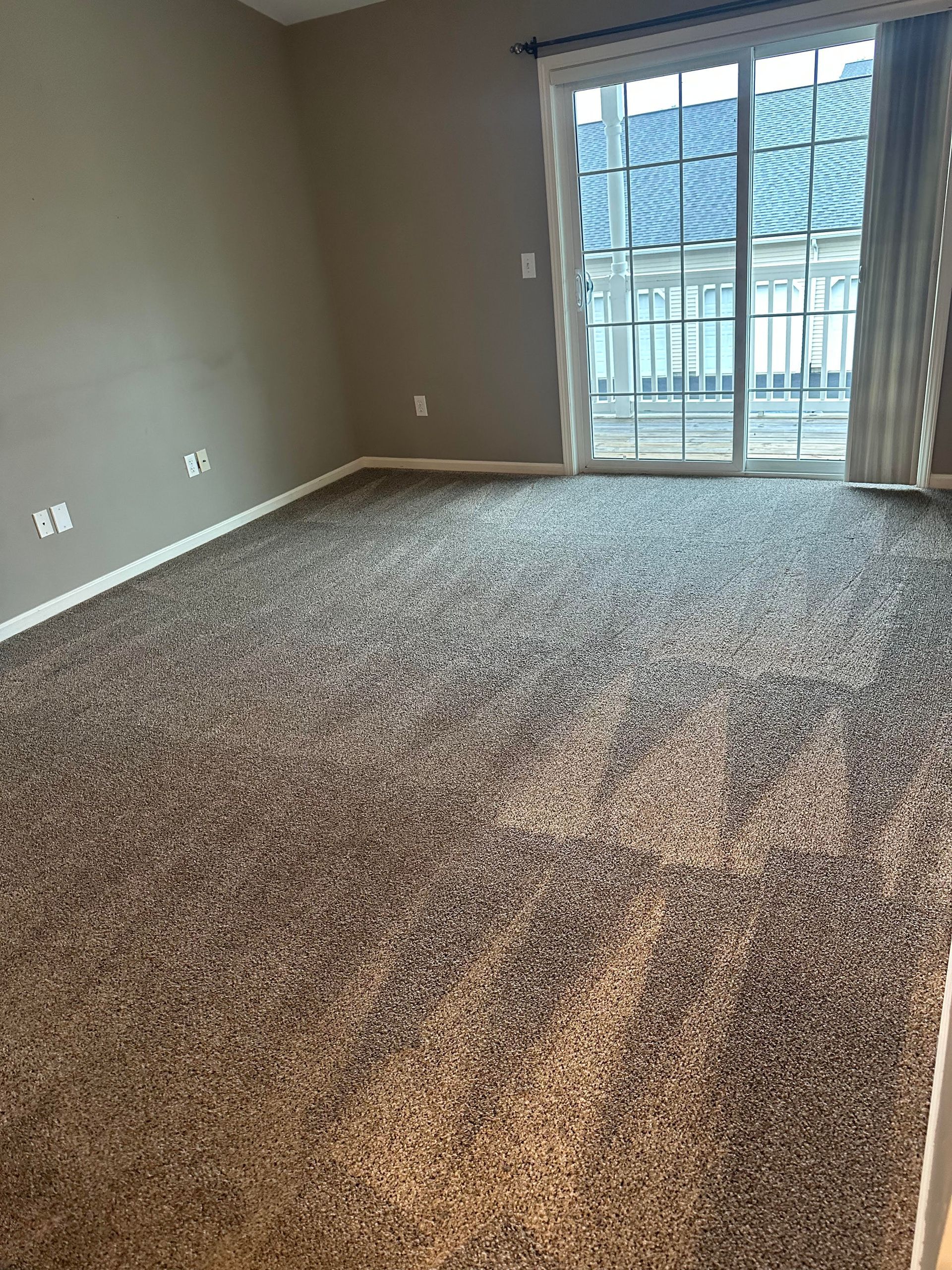 An empty living room with a large carpet and a sliding glass door.