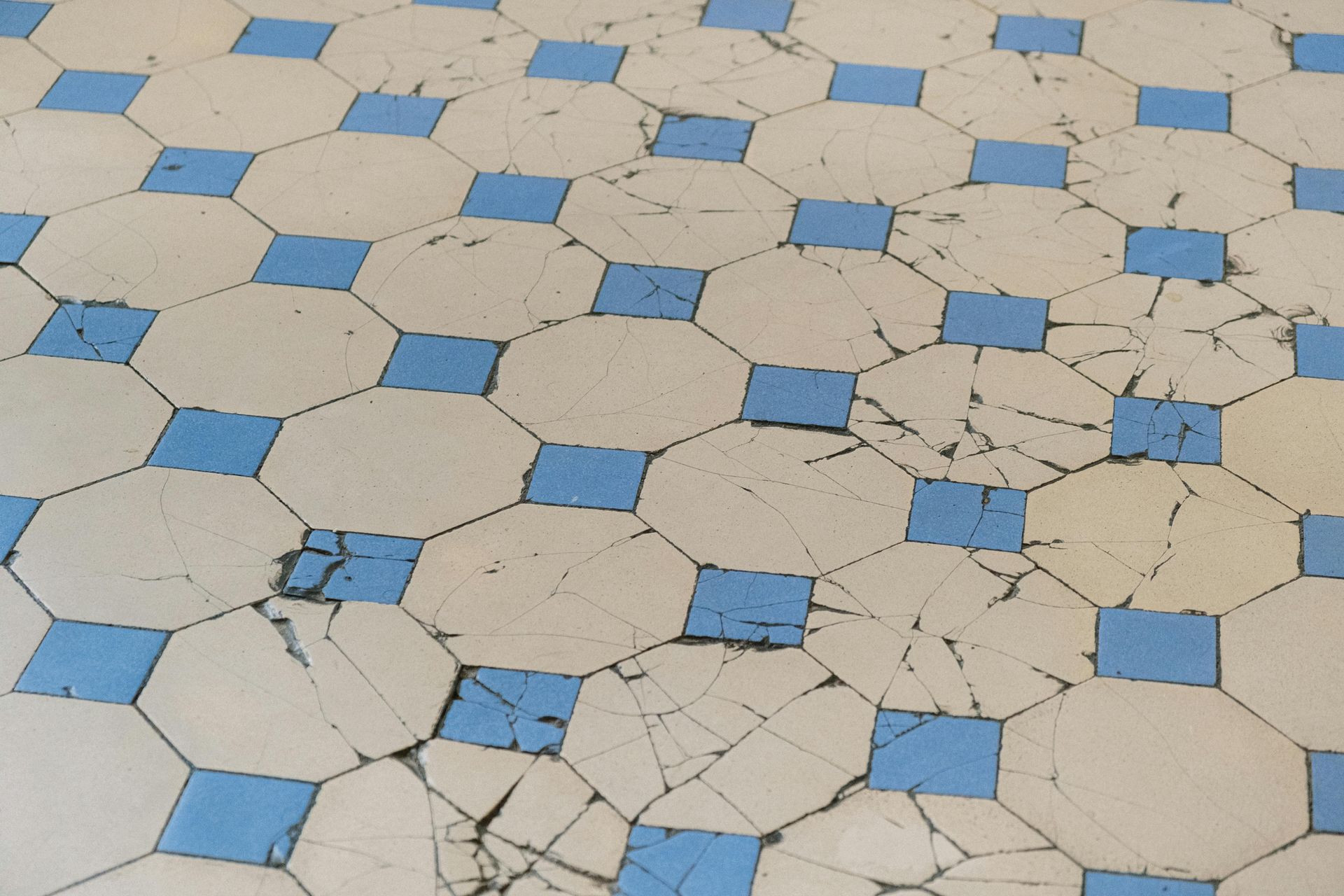 Cracked, worn tile floor. Pattern of blue squares interspersed with off-white octagons.