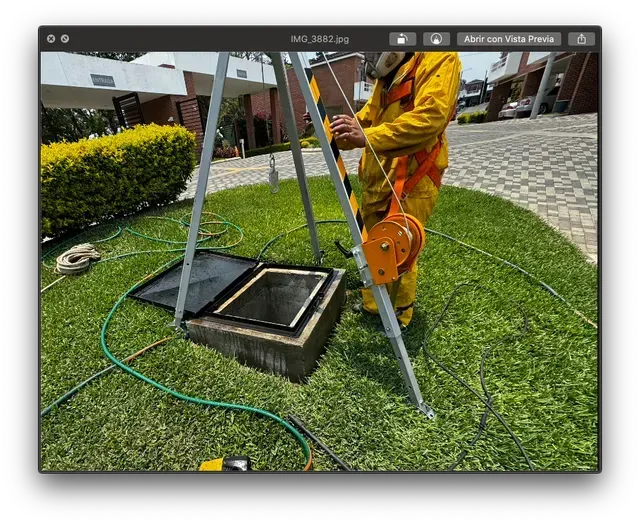 Un trabajador con ropa naranja utiliza una bomba en un pozo cuadrado en el césped de un patio.