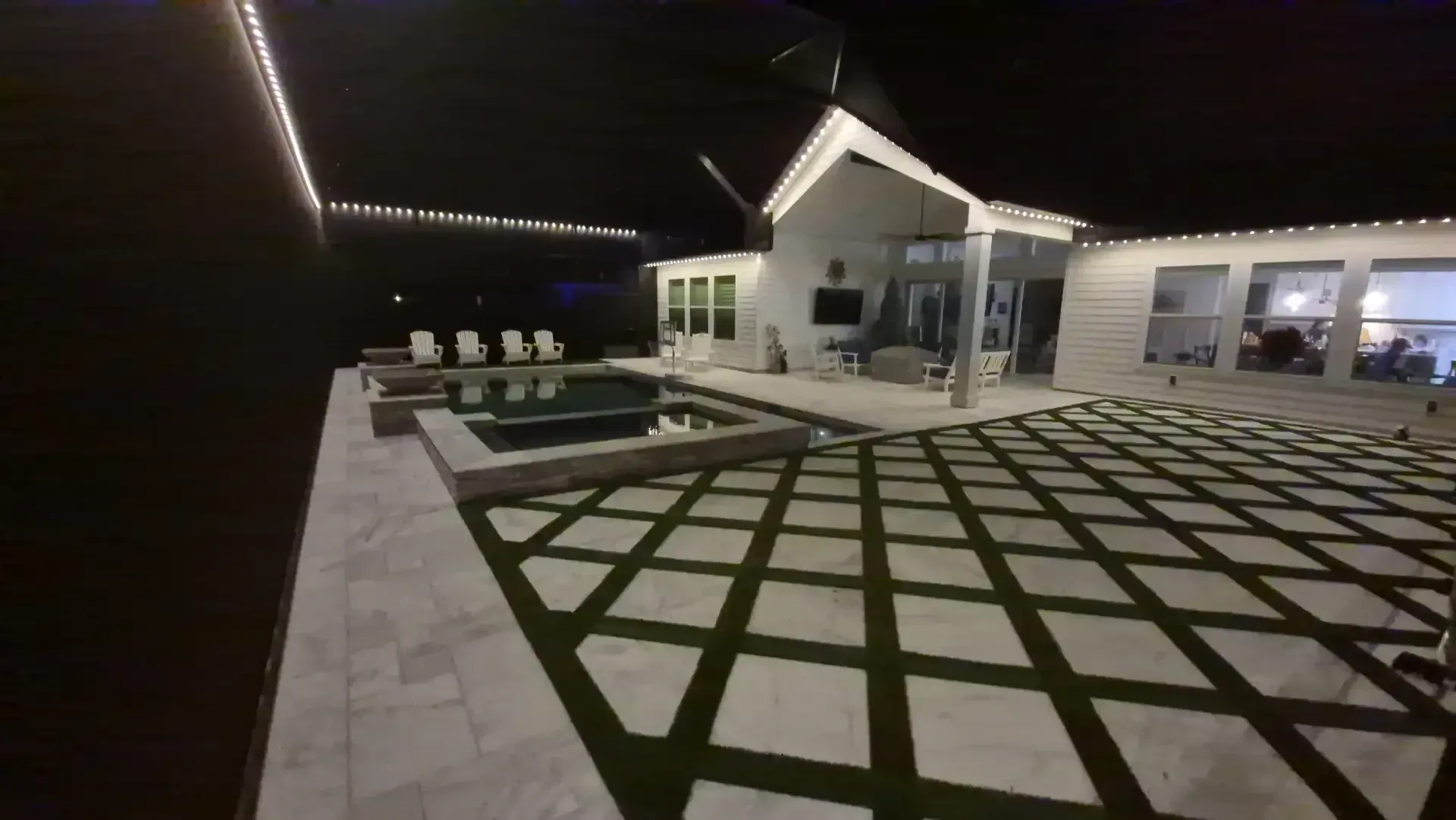 Modern backyard patio with pool and warm outdoor lighting at night