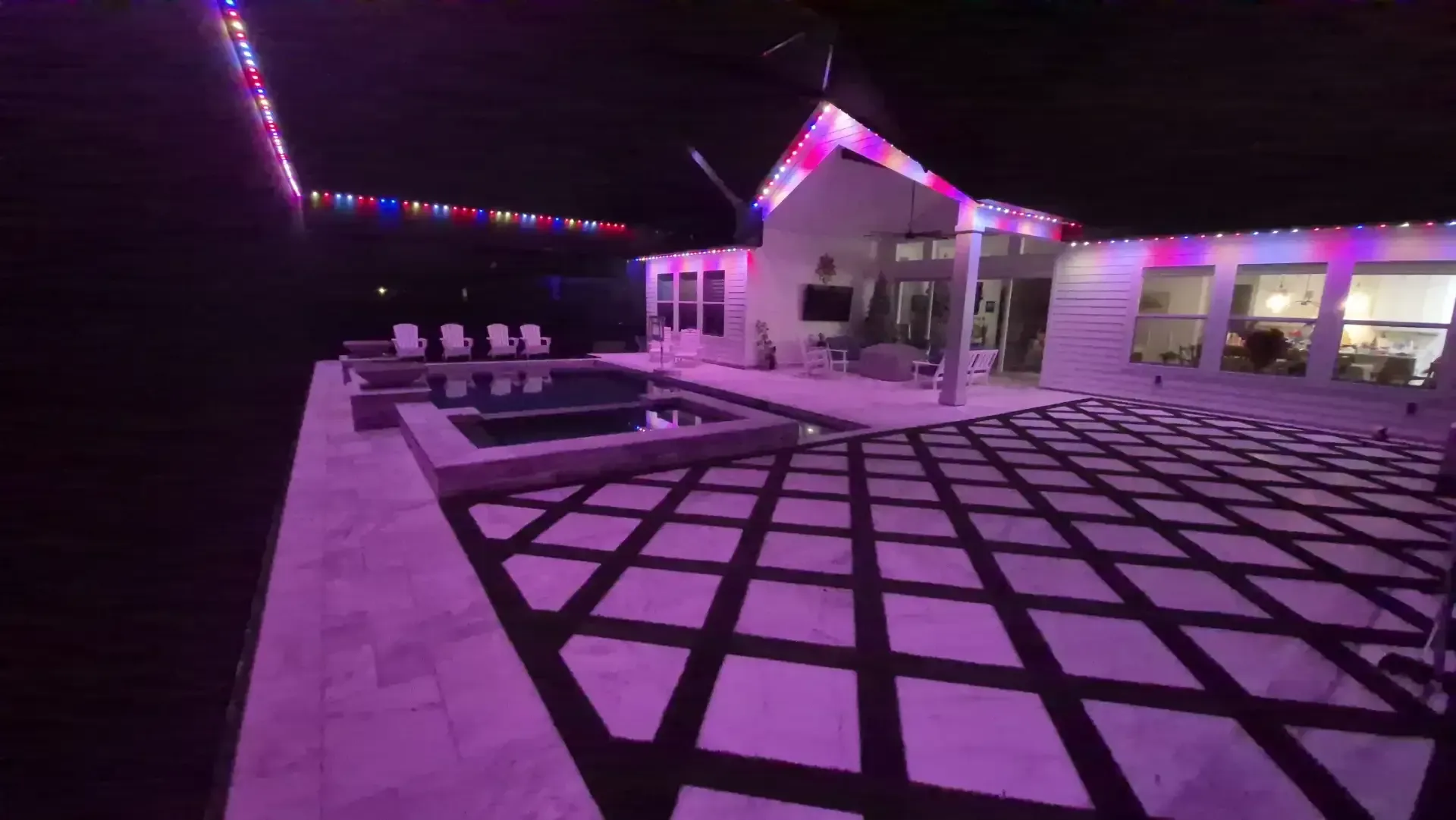 Backyard pool area with colorful LED lighting around a modern home at night
