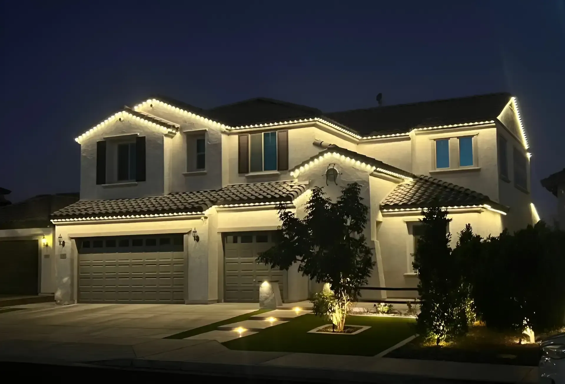 Two-story home with garden and pathway lighting at night