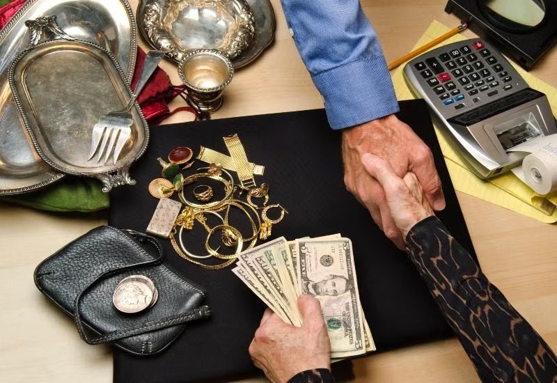 Hands counting cash beside jewelry, wallets, and a calculator on a table