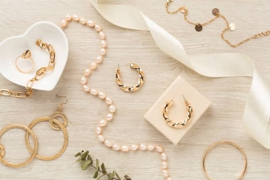 Gold and pearl jewelry arranged on a soft cream background with decorative leaves and trays