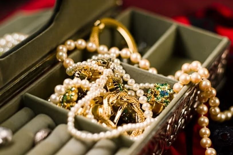 Gold and pearl jewelry tangled in a green velvet box with a red interior