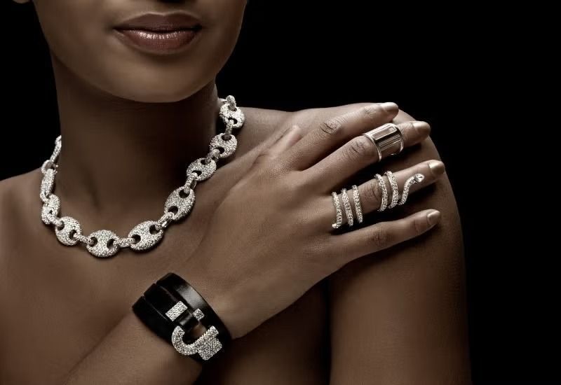 Close-up of a model wearing silver necklace, rings, and bracelet on a dark background