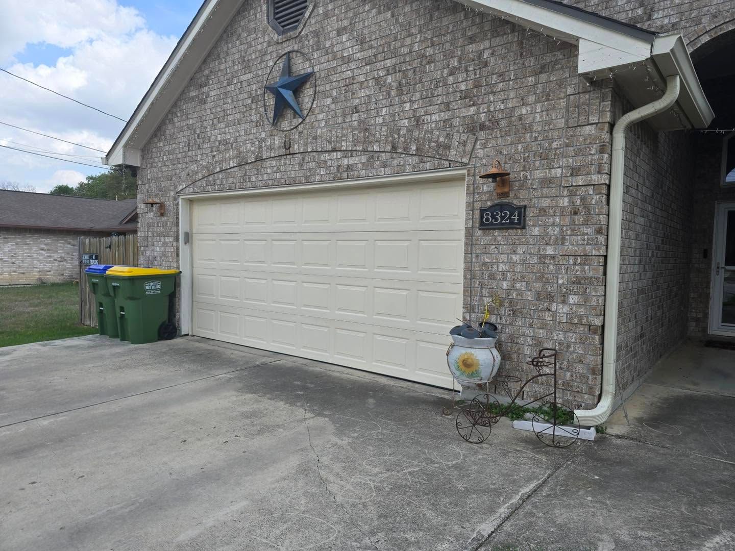 Brick house garage with white door, star wall decor, and trash bins by the driveway