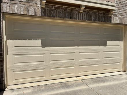 Closed beige garage door on a brick building, viewed from a driveway.