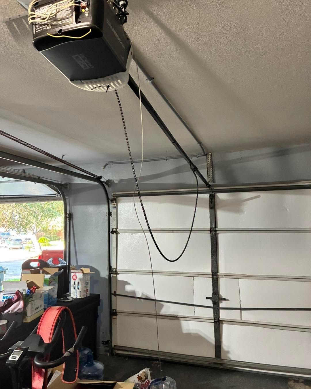 Garage interior with open garage door, ceiling opener, hanging cord, and workbench at left.