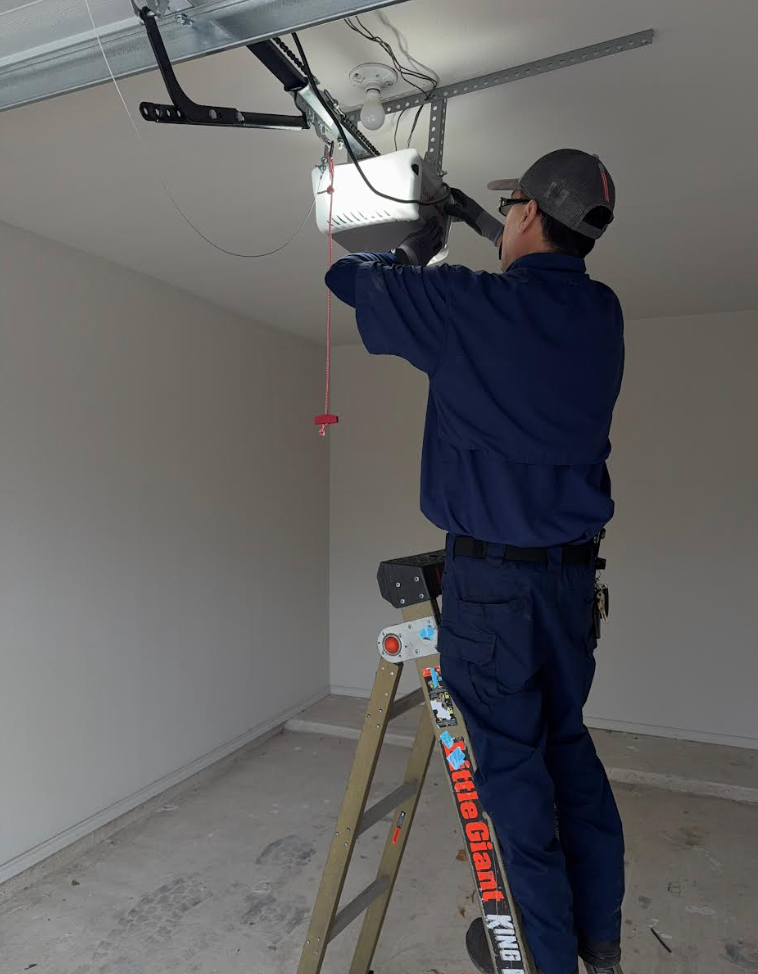 Worker on a ladder installing a garage door opener in a bare garage.