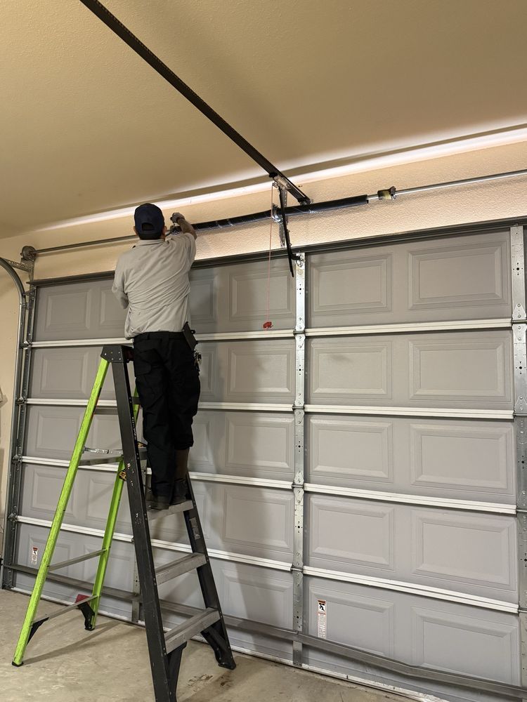 Person on a ladder adjusting a garage door opener track inside a garage.