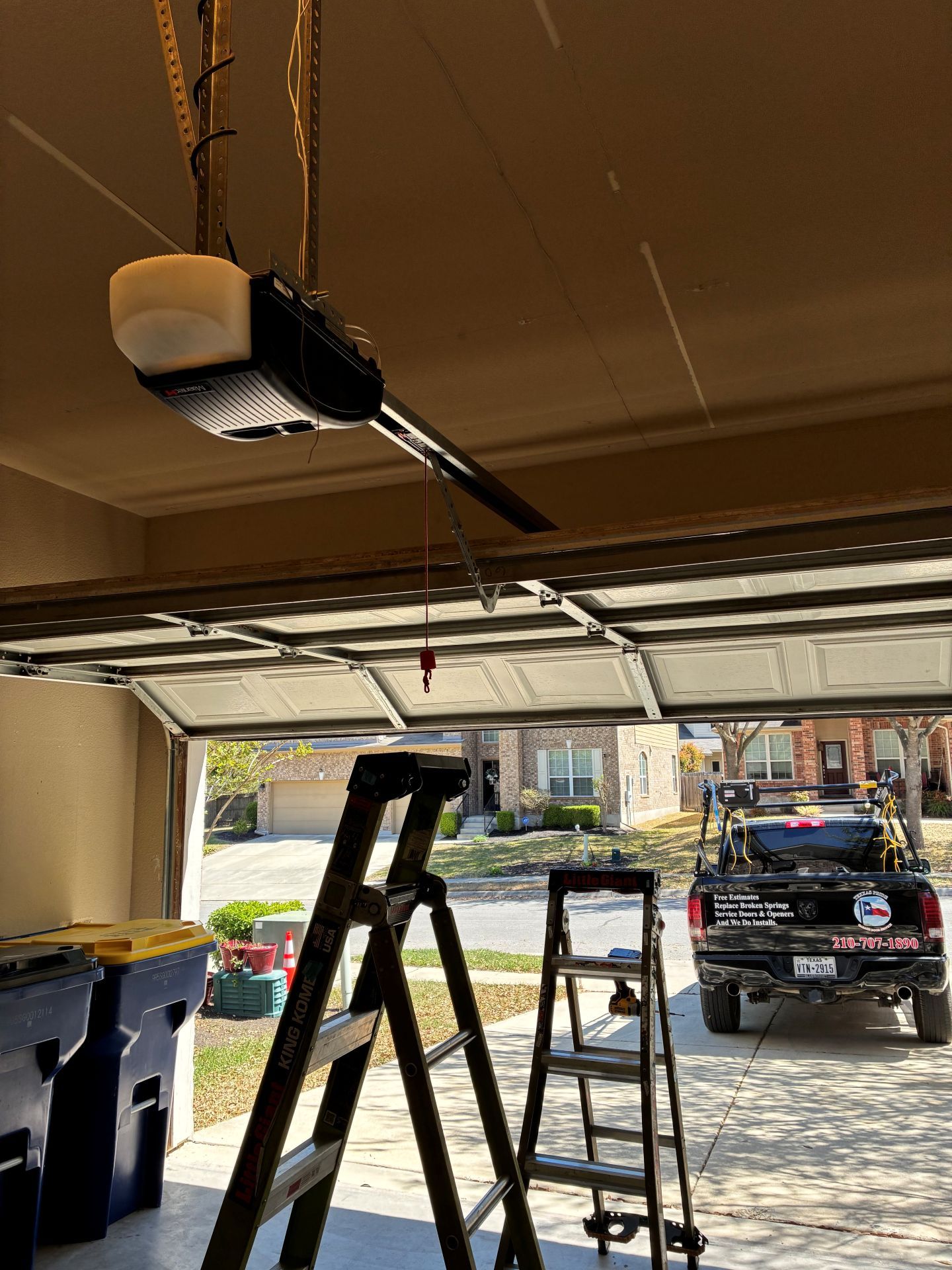 Garage with open door, ladder, and ceiling-mounted garage door opener above a parked truck.