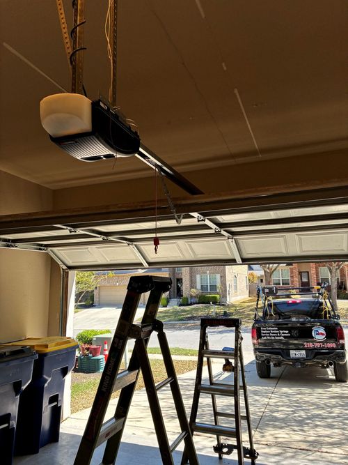 Garage with an open door, ladder, and garage door opener installed overhead.