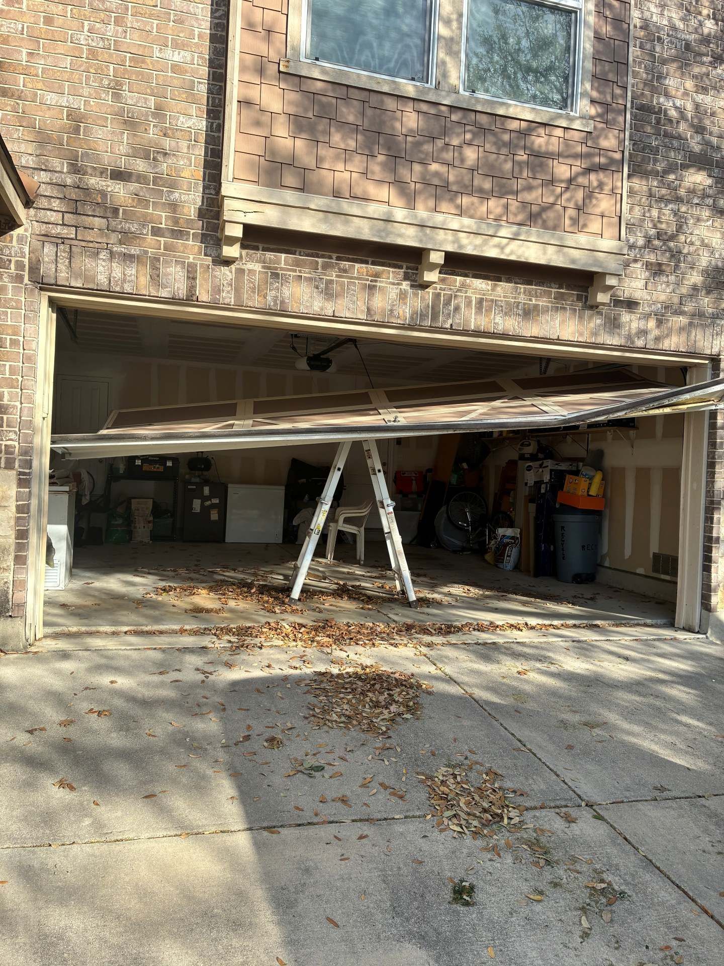 Detached garage door bent open with a ladder inside a brick apartment building.