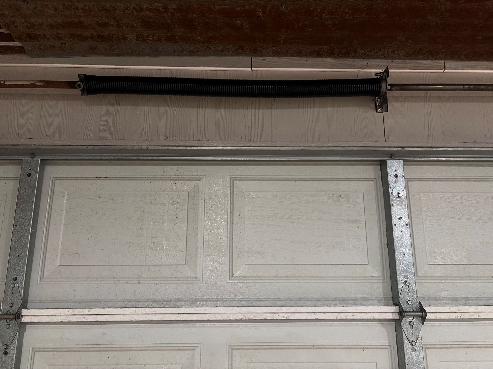 Closed white garage door with a vertical metal track and opener rail above it