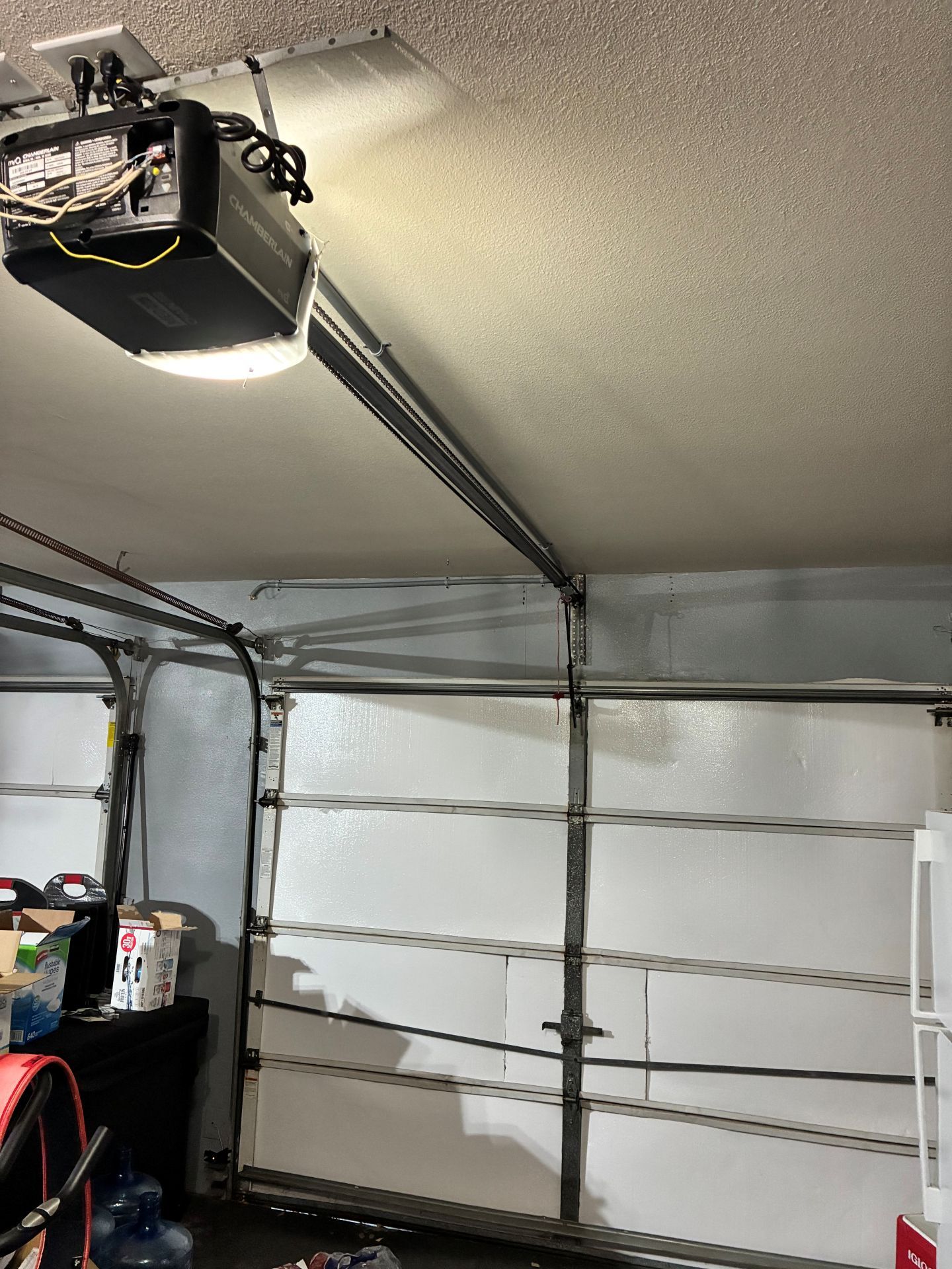 Inside a garage, a white sectional garage door, opener, and wall-mounted shelves are visible.
