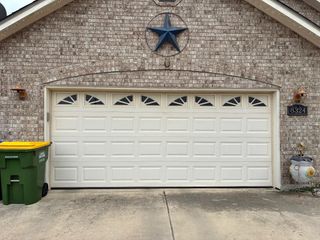 White garage door on a stone house with a blue star above it, green trash bins on the left.