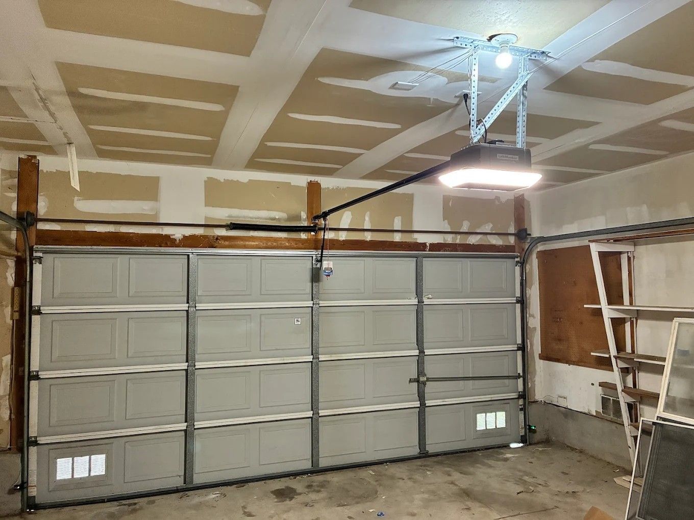 Garage interior with closed gray sectional door, unfinished drywall, and overhead opener.