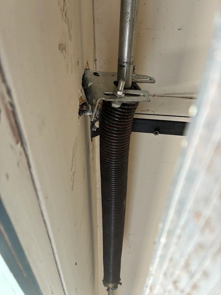 Black garage door torsion spring mounted on a metal shaft against a beige wall.
