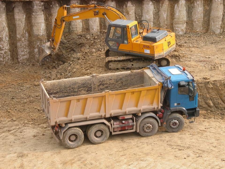 Yellow excavator loading dirt into blue dump truck at a construction site