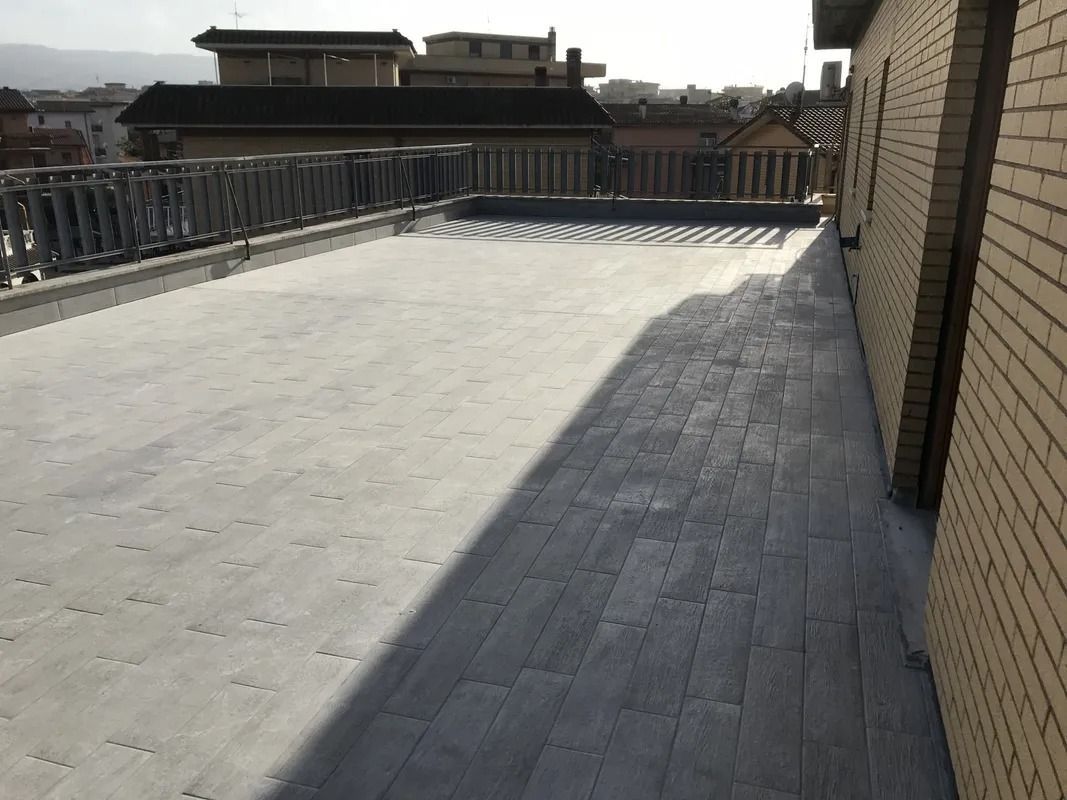 Rooftop terrace with metal railings, brick wall, and bright sunlit concrete floor.