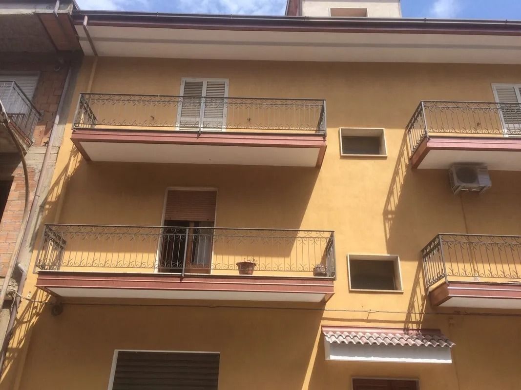 Yellow apartment building with balconies, windows, and awnings under a bright sky