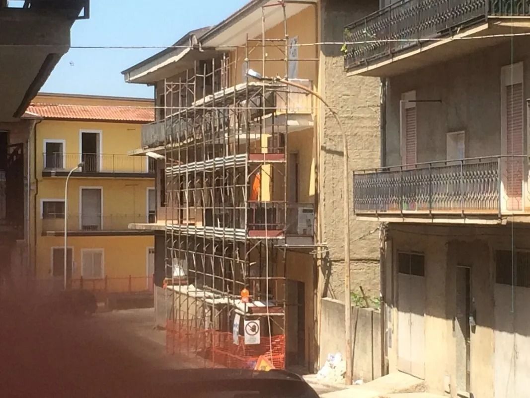 Apartment buildings with scaffolding on a sunny street, and a worker in orange near the center.